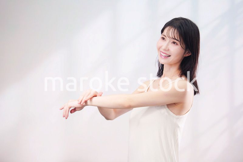 腕にクリームを塗る若い女性（シンプル背景）