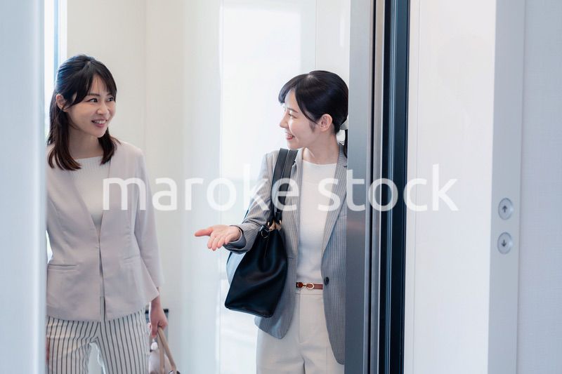 エレベーターで譲り合う2人のビジネスパーソン