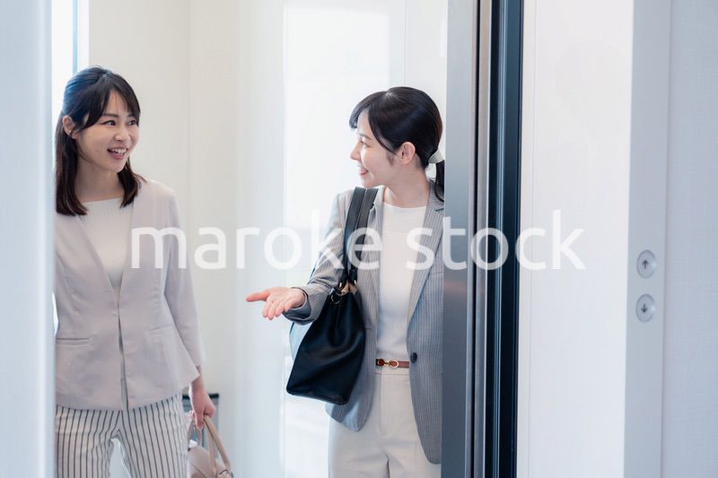 エレベーターで譲り合う2人のビジネスパーソン