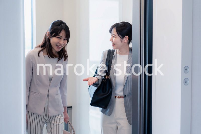 エレベーターで譲り合う2人のビジネスパーソン