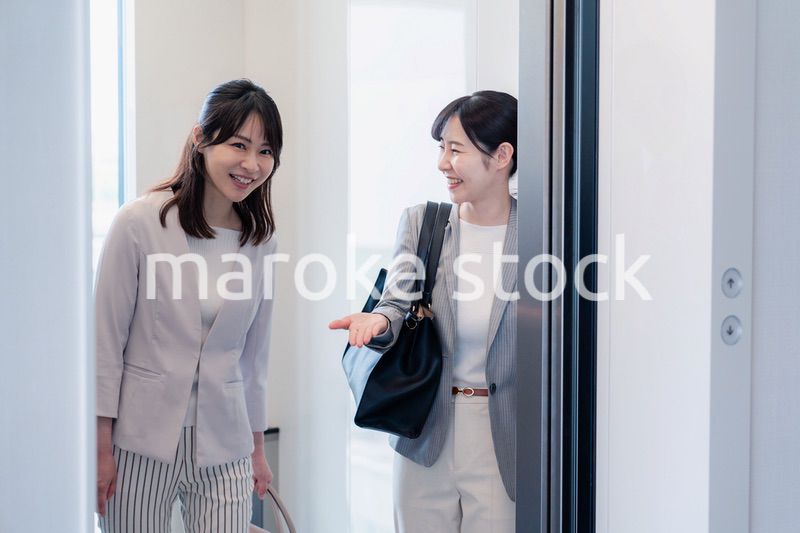 エレベーターで譲り合う2人のビジネスパーソン