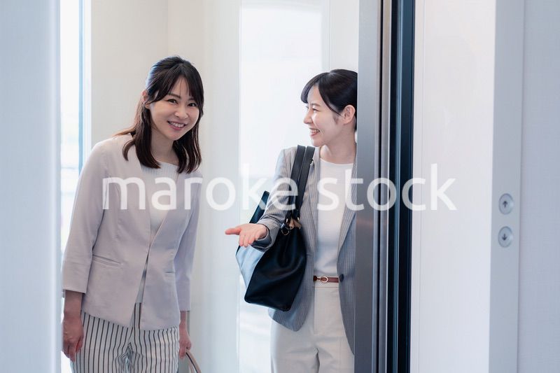 エレベーターで譲り合う2人のビジネスパーソン