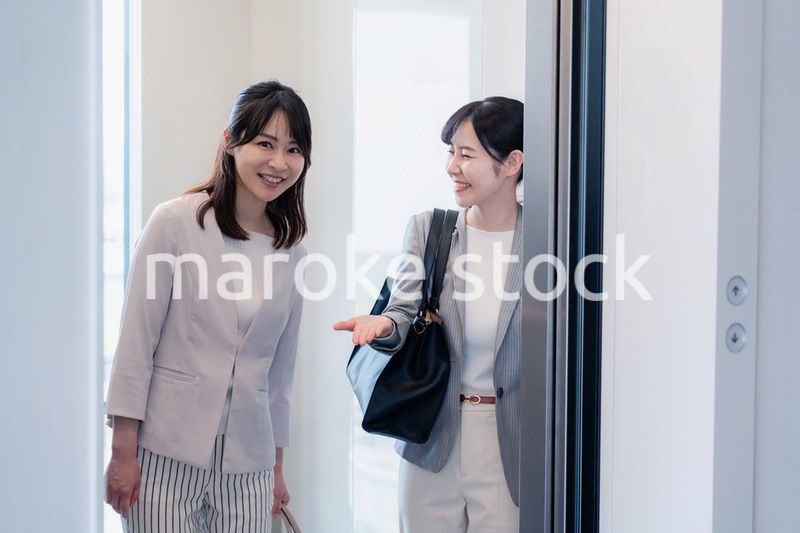 エレベーターで譲り合う2人のビジネスパーソン