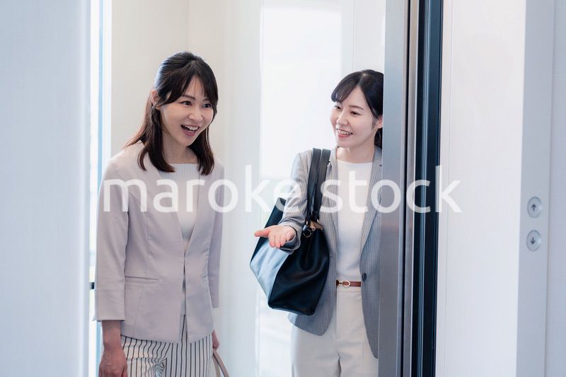 エレベーターで譲り合う2人のビジネスパーソン