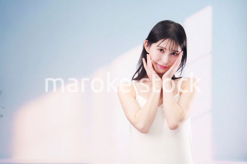 笑顔でお肌のケアをする若い女性（シンプル背景）