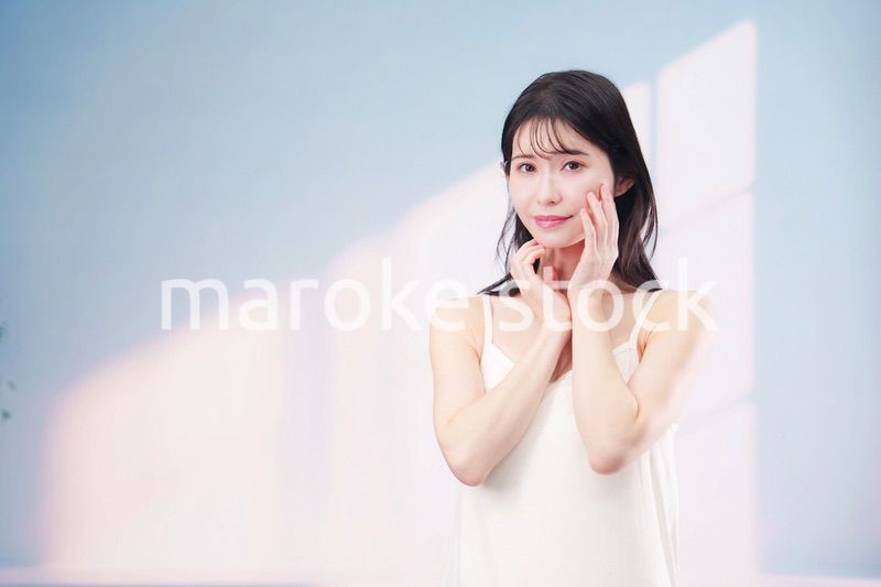 笑顔でお肌のケアをする若い女性（シンプル背景）