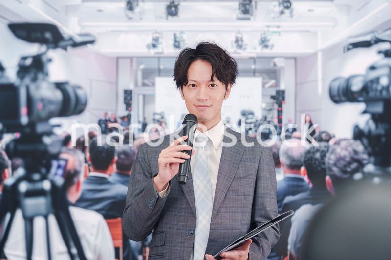 メディアが多く集まる記者会見会場で話す男性