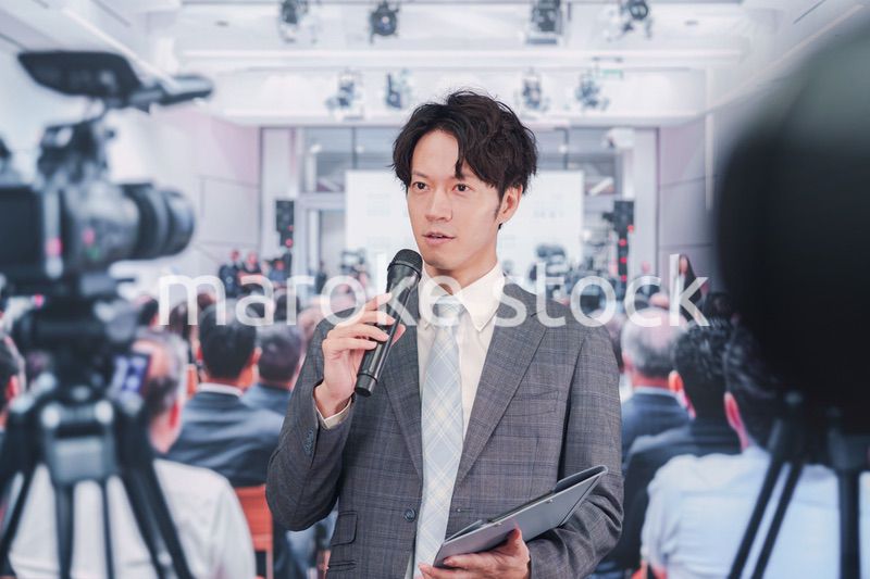 メディアが多く集まる記者会見会場で話す男性