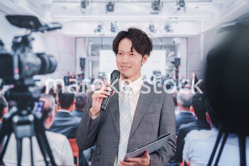 メディアが多く集まる記者会見会場で話す男性