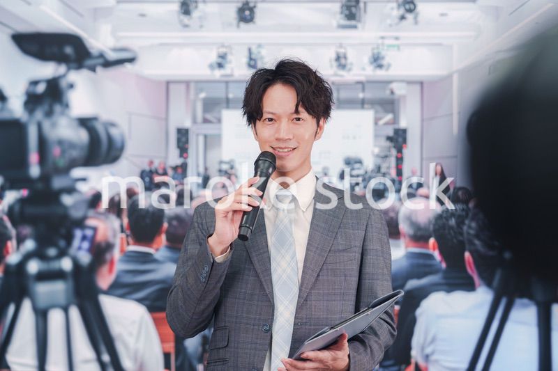 メディアが多く集まる記者会見会場で話す男性