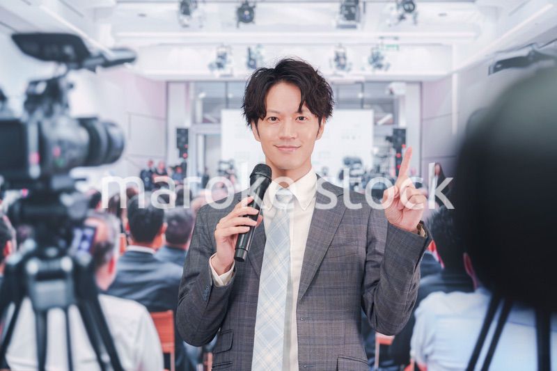 メディアが多く集まる記者会見会場で話す男性