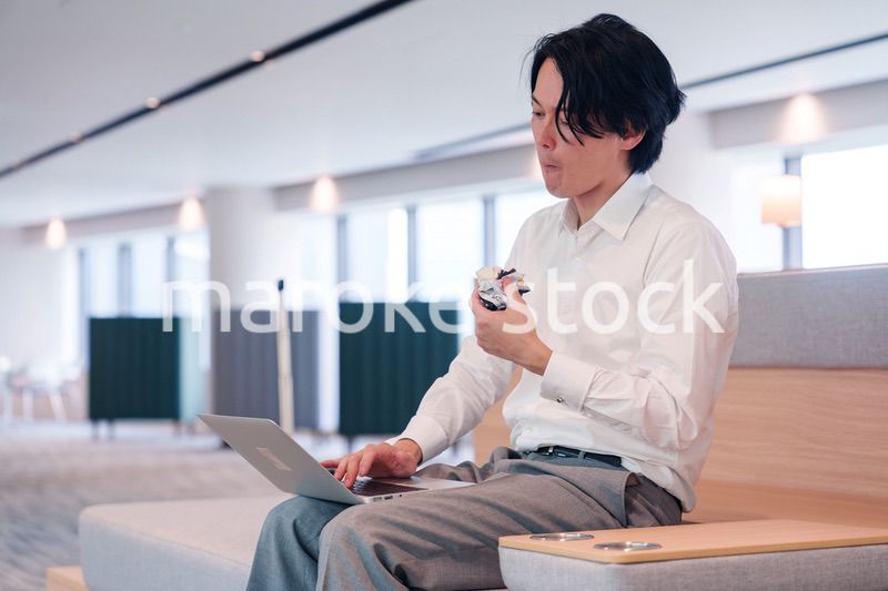 お昼ごはんを食べながらオフィスで仕事をする男性