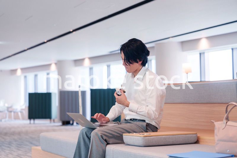 お昼ごはんを食べながらオフィスで仕事をする男性