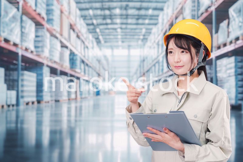 大きな物流倉庫で働くヘルメットを被った若い女性