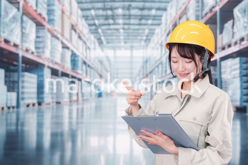 大きな物流倉庫で働くヘルメットを被った若い女性