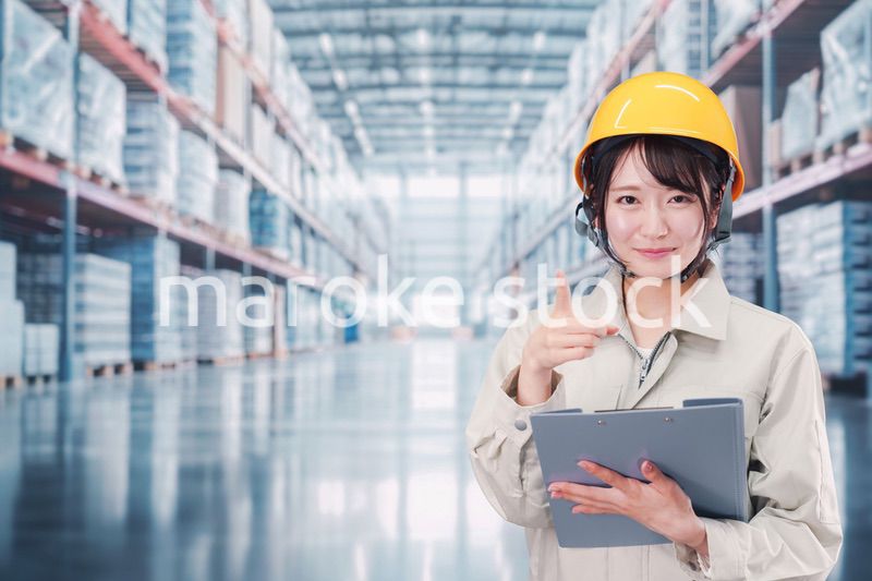 大きな物流倉庫で働くヘルメットを被った若い女性