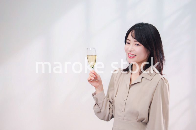 笑顔でスパークリングワインを飲む若い女性（シンプル背景）