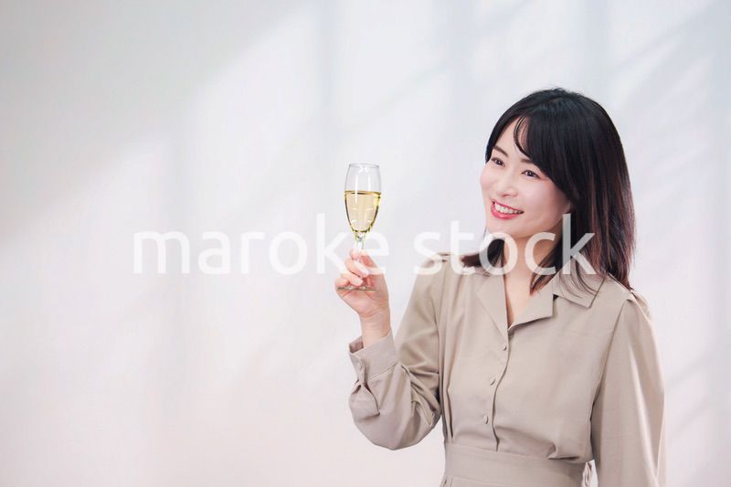 笑顔でスパークリングワインを飲む若い女性（シンプル背景）
