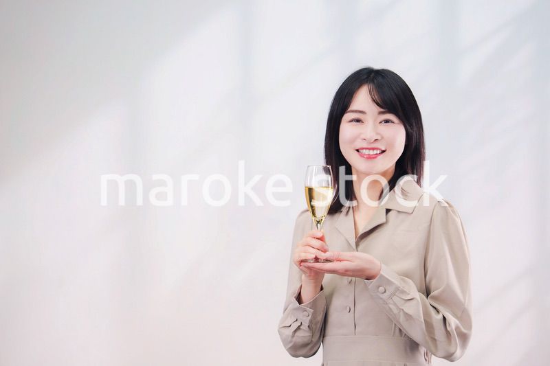 笑顔でスパークリングワインを飲む若い女性（シンプル背景）