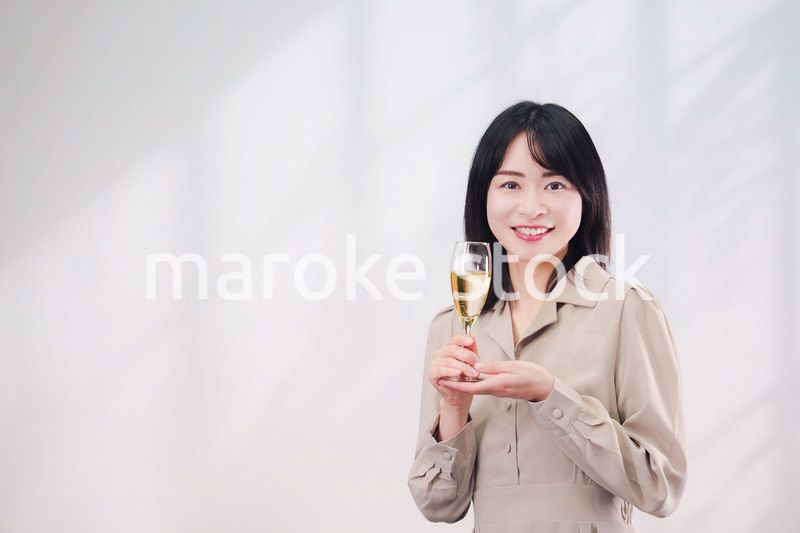 笑顔でスパークリングワインを飲む若い女性（シンプル背景）