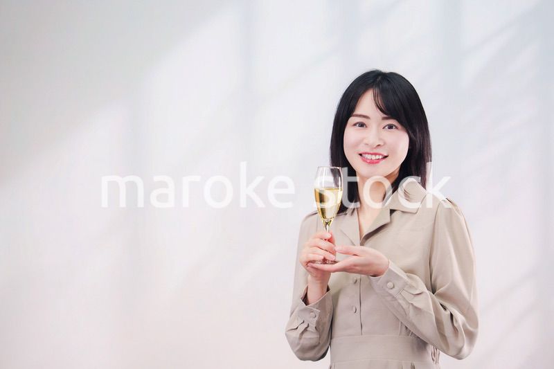 笑顔でスパークリングワインを飲む若い女性（シンプル背景）