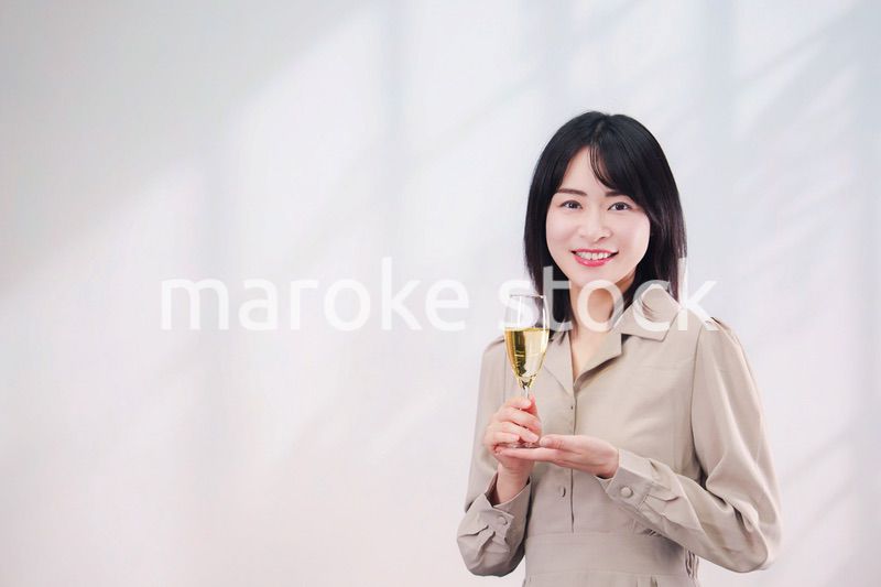 笑顔でスパークリングワインを飲む若い女性（シンプル背景）