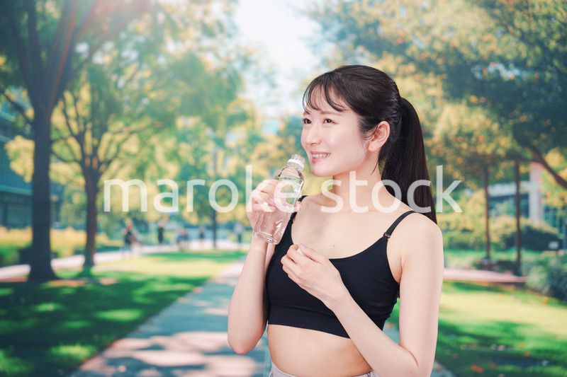 外でランニングをしながら水を飲む若い女性