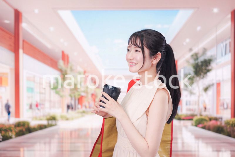 コーヒーを飲みながらショッピングモールで買い物をする女性
