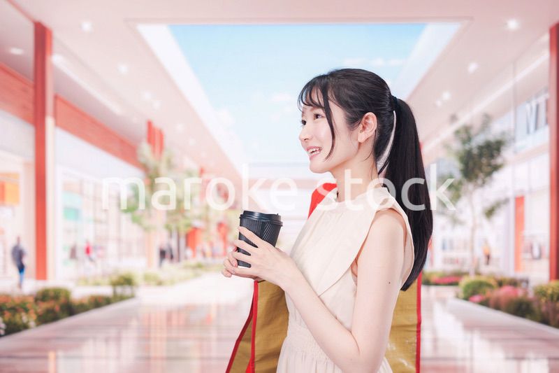 コーヒーを飲みながらショッピングモールで買い物をする女性