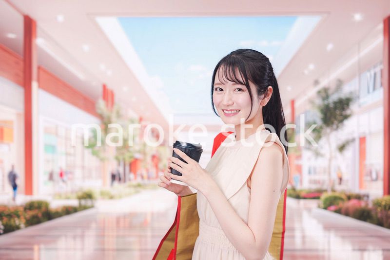 コーヒーを飲みながらショッピングモールで買い物をする女性