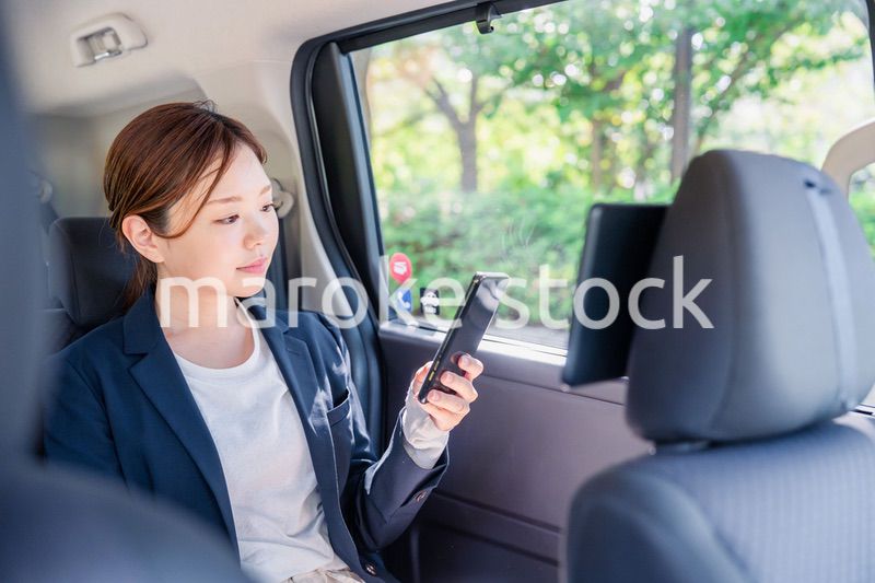 タクシーでスマホを使う若い女性ビジネスパーソン