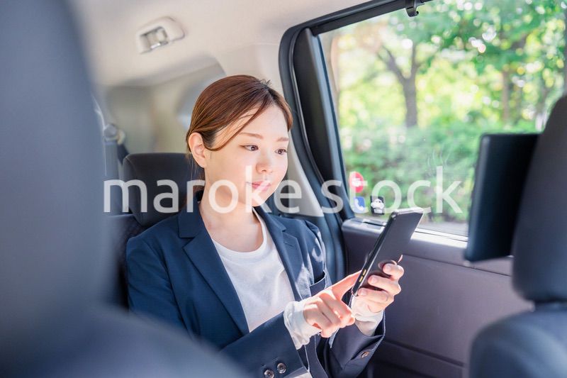 タクシーでスマホを使う若い女性ビジネスパーソン