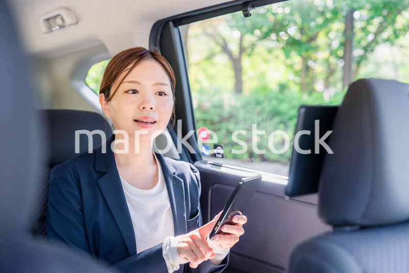 タクシーでスマホを使う若い女性ビジネスパーソン