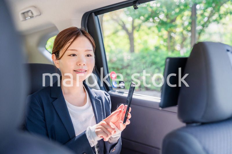 タクシーでスマホを使う若い女性ビジネスパーソン
