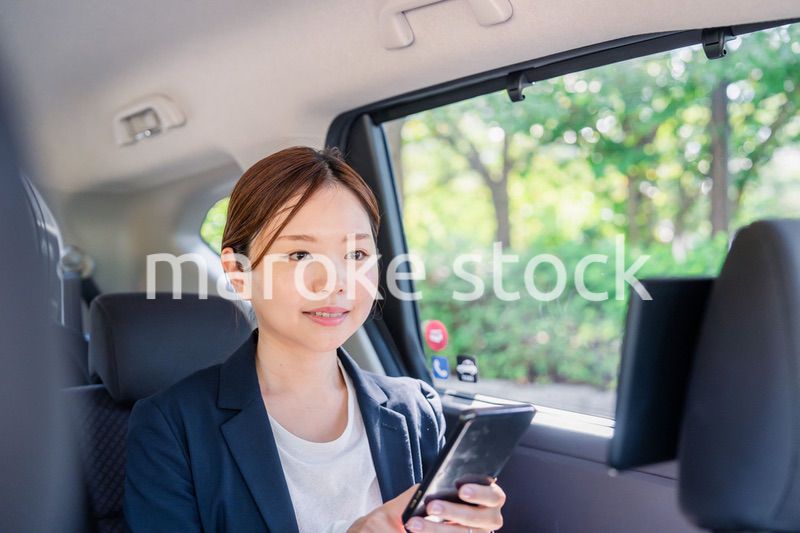 タクシーでスマホを使う若い女性ビジネスパーソン