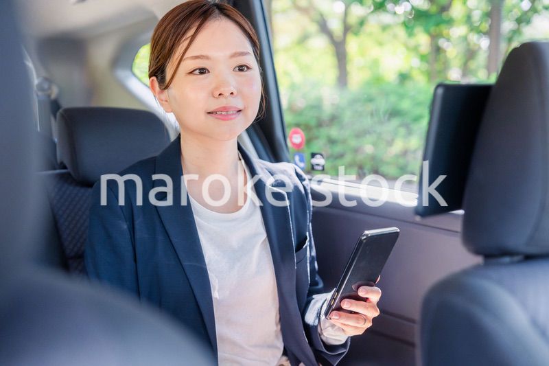 タクシーでスマホを使う若い女性ビジネスパーソン