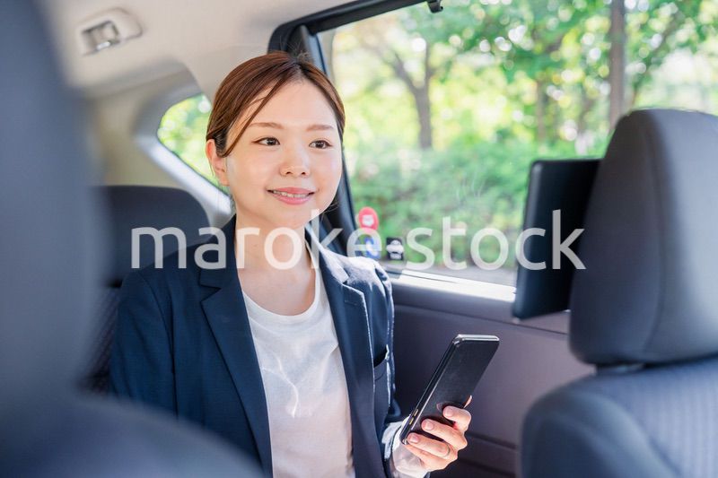 タクシーでスマホを使う若い女性ビジネスパーソン