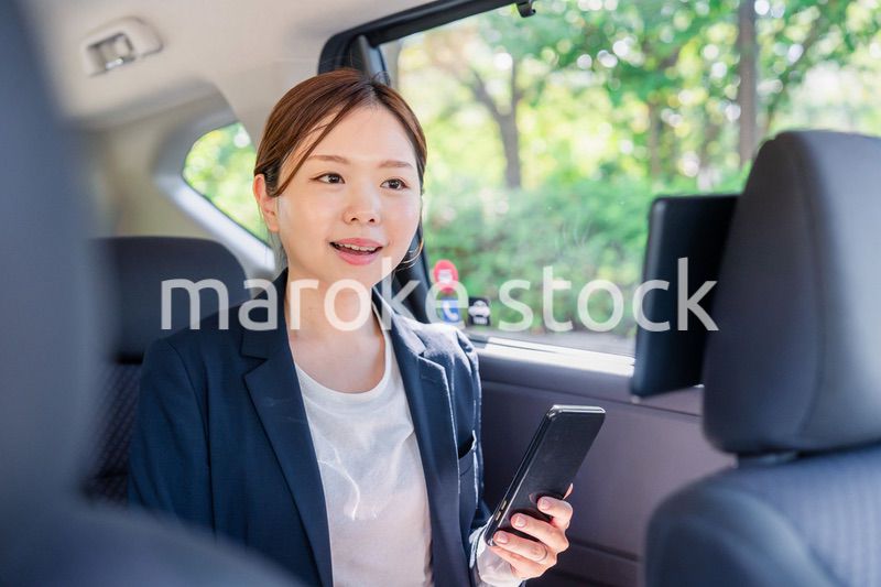 タクシーでスマホを使う若い女性ビジネスパーソン