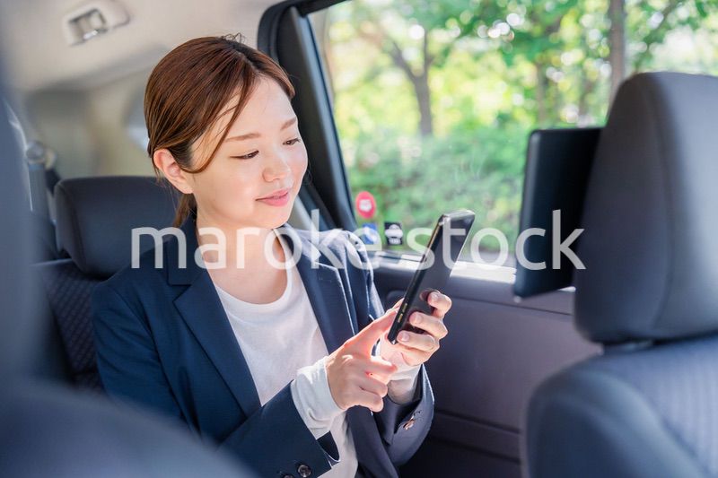 タクシーでスマホを使う若い女性ビジネスパーソン