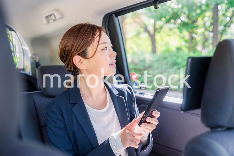 タクシーでスマホを使う若い女性ビジネスパーソン