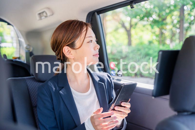 タクシーでスマホを使う若い女性ビジネスパーソン