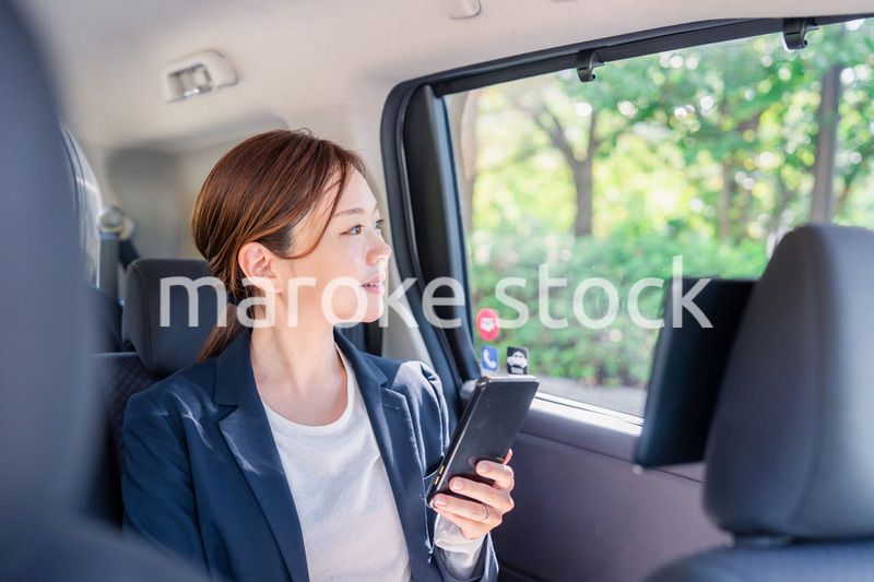 タクシーでスマホを使う若い女性ビジネスパーソン