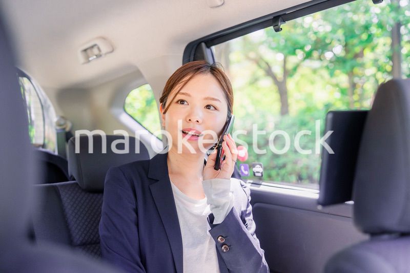 タクシーに乗って電話をする若い営業の女性
