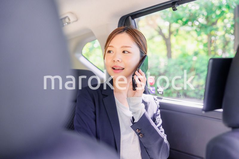 タクシーに乗って電話をする若い営業の女性