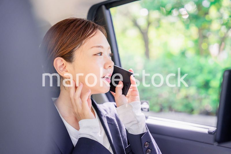 タクシーに乗って電話をする若い営業の女性