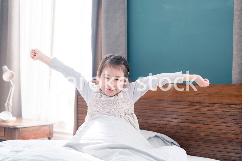 朝ベッドで目覚めて伸びをする小さな女の子