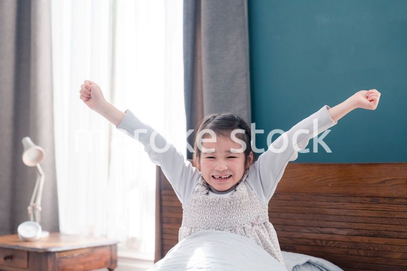 朝ベッドで目覚めて伸びをする小さな女の子