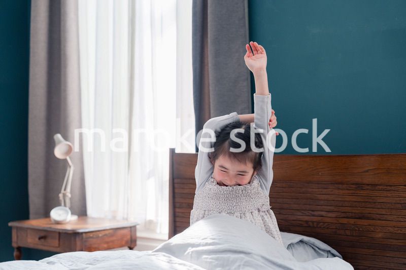朝ベッドで目覚めて伸びをする小さな女の子