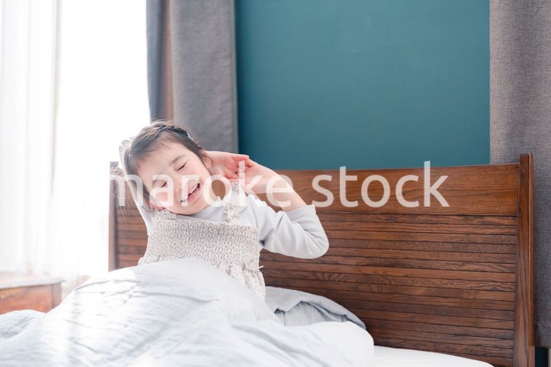 朝ベッドで目覚めて伸びをする小さな女の子