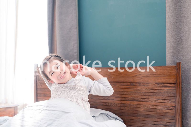 朝ベッドで目覚めて伸びをする小さな女の子